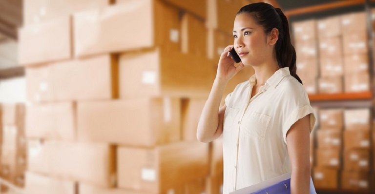 A businesswoman is standing in a stockroom and talking on the phone.
