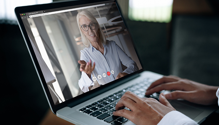 A businessman speaks on a web conference with an advisor using a laptop webcam.