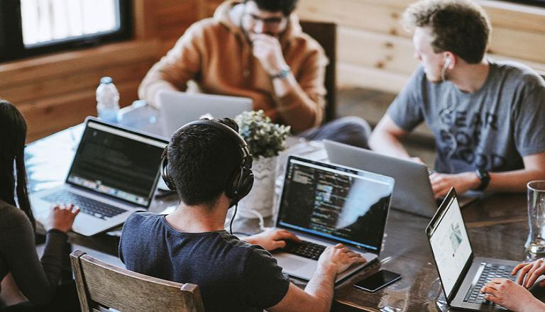 Cinq personnes à leurs portables échangent des idées dans un espace de travail partagé.