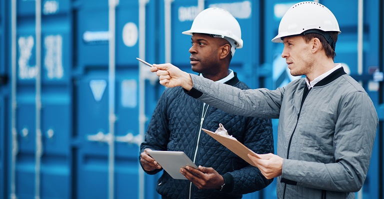Two businessmen in hard hats with shipping containers in background